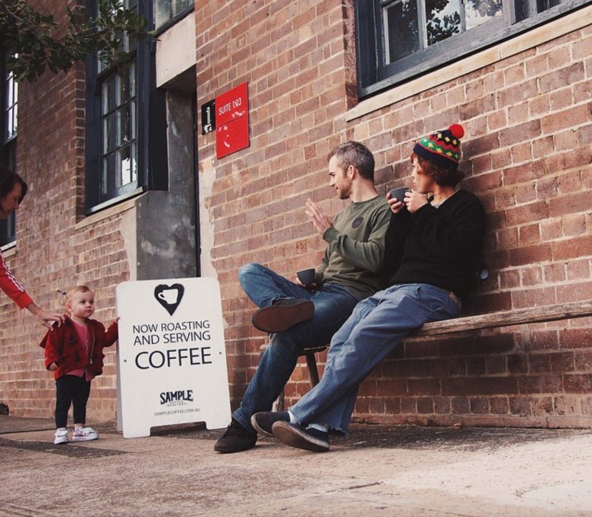 Reuben and staff member have coffee outside our coffee shop and wave to a toddler and mum pasing by.