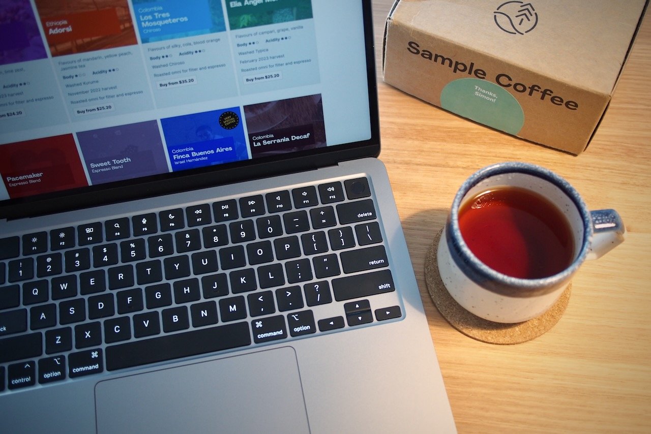 Laptop showing Sample Coffee website, sitting on a table next to a speckled ceramic mug with coffee